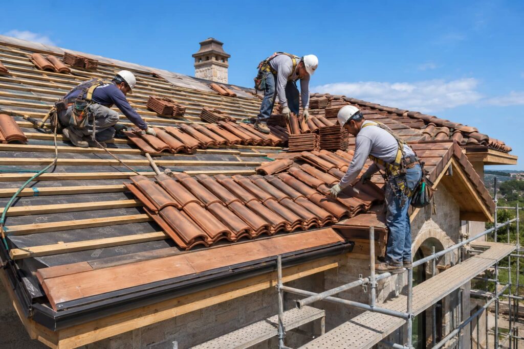 Roofing contractors installing clay roof tiles on a residential home.